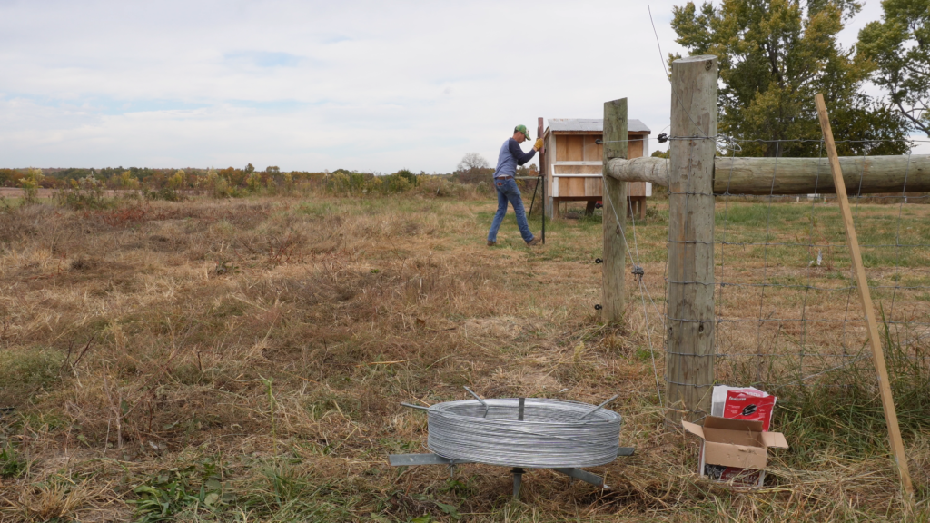 man driving a t post building fence in a pasture