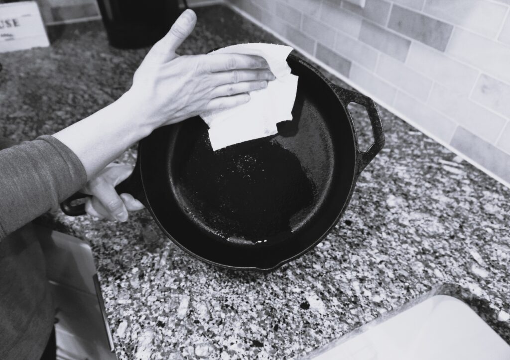 wiping the inside of a cast iron skillet with a paper towel