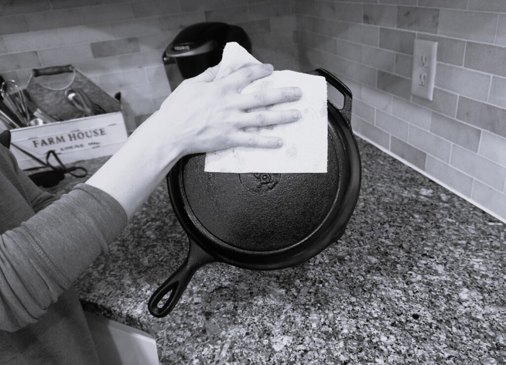 wiping the outside of a cast iron skillet with a paper towel