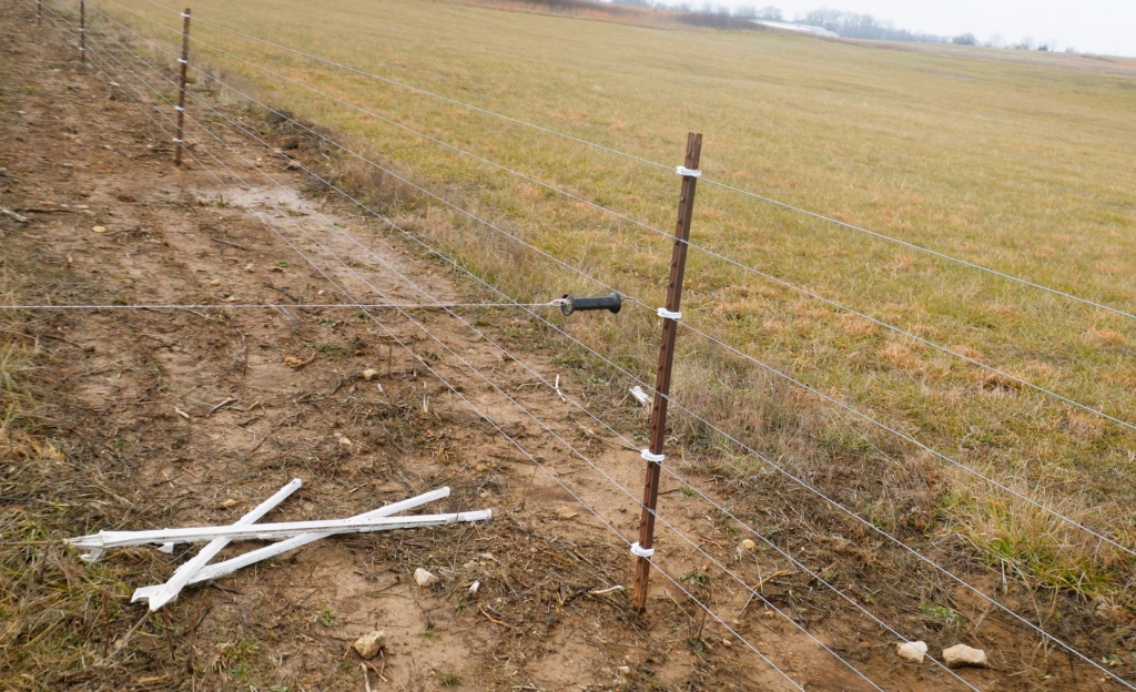 electric fence with poly wire running off the fence and a pile of tread in post on the ground