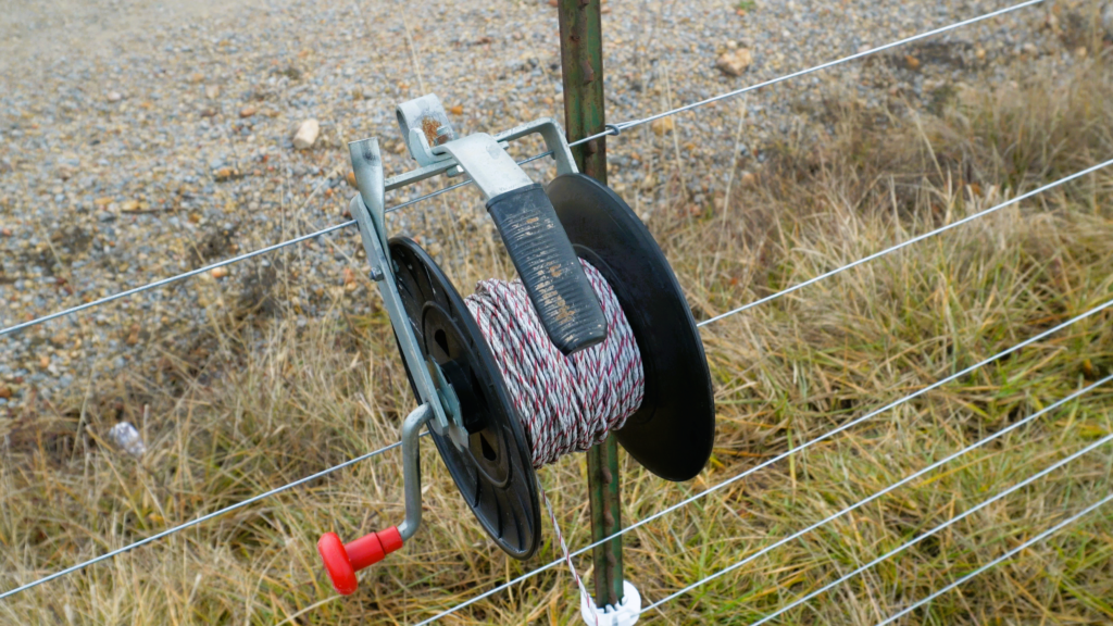reel of poly wire hanging on an electric fence