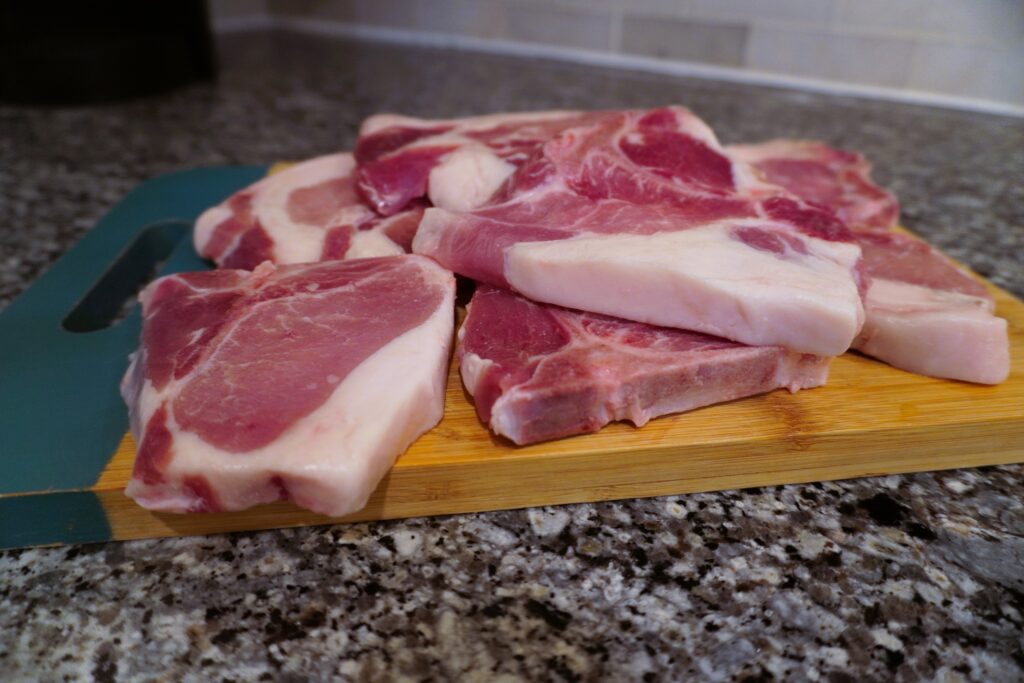 raw pork chops stacked on a cutting board