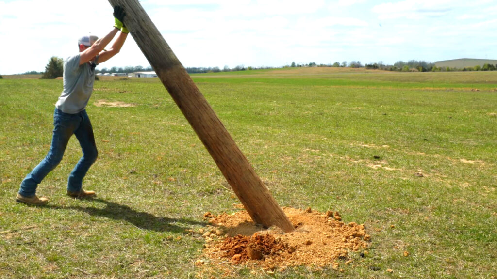 Man in a field pushing up a telephone pole