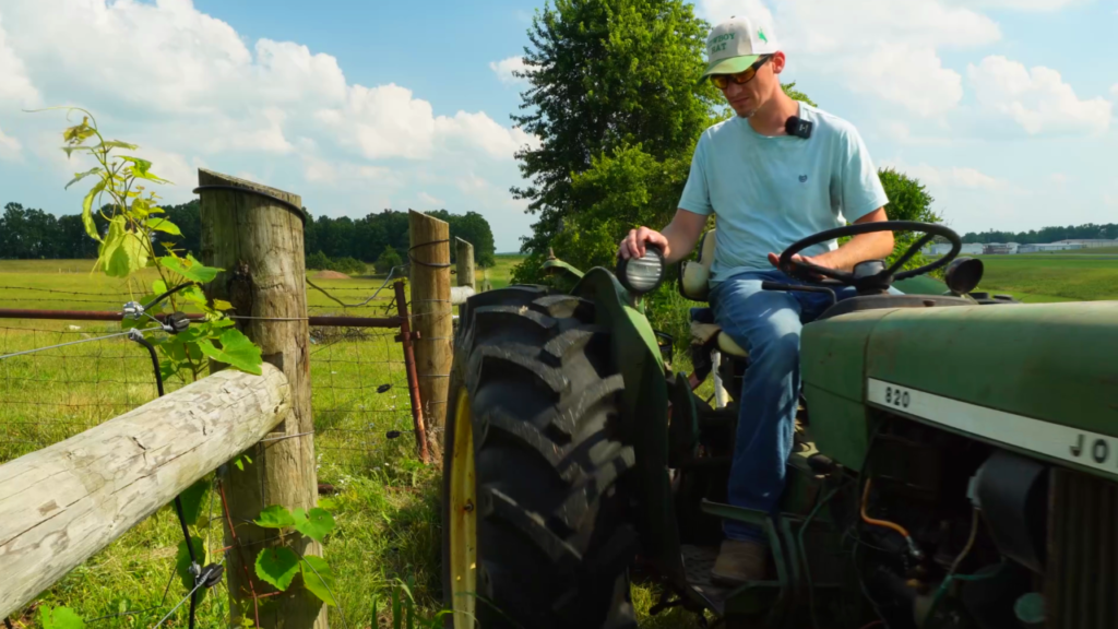 Man on a green tractor in a field by a fence line