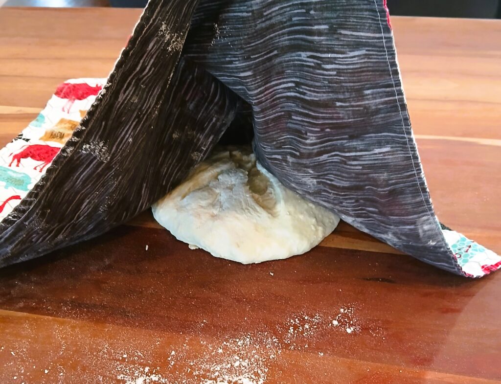 A bowl of dough on a counter being covered by a towel