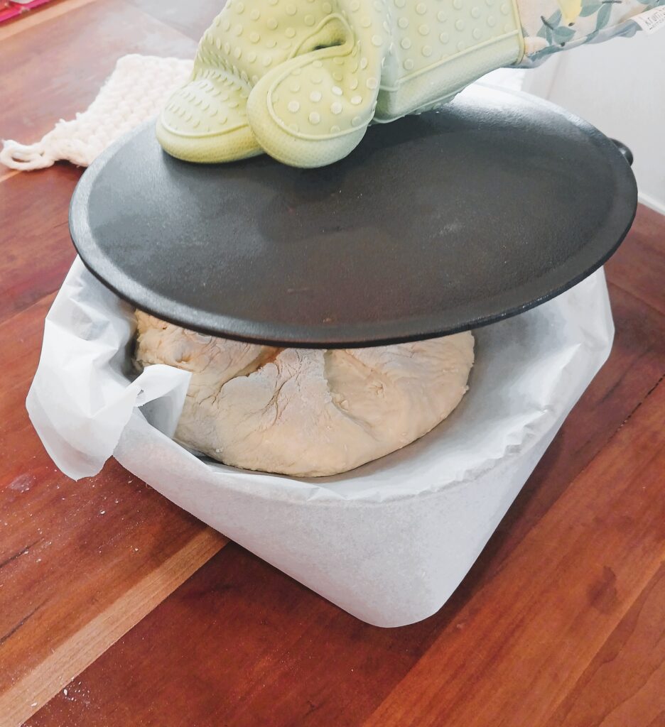 Dough in a cast iron Dutch oven being covered with the lid