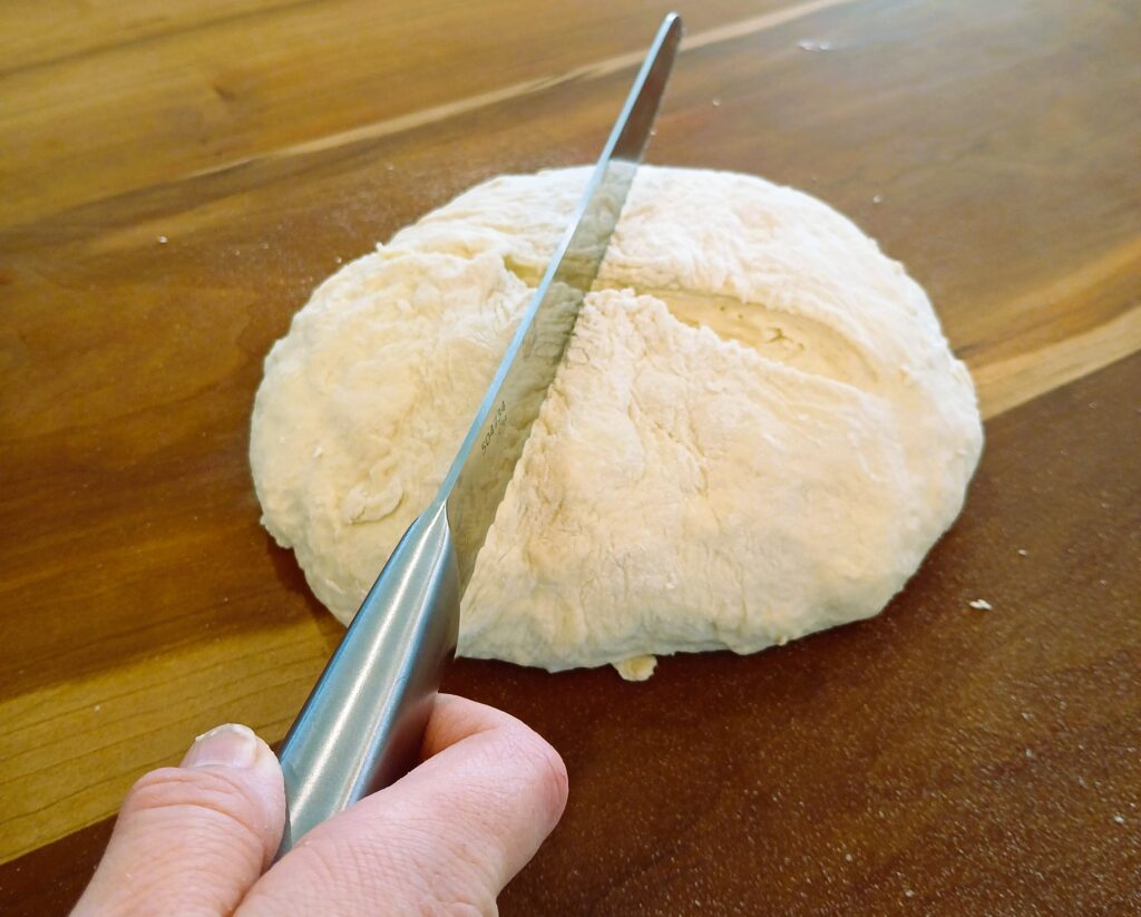 A knife being used to cut a shape in a ball of dough for Artisan Bread