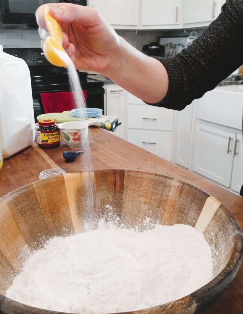 Salt being poured into flour mixture in a wooden bowl