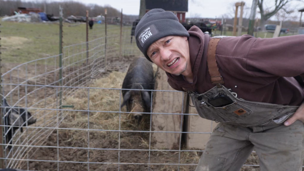 Man looking at a camera with a black pig in the background