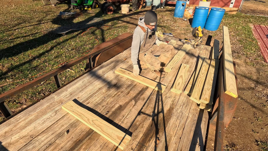 Man sitting on a trailer putting boards together for a DIY round bale feeder