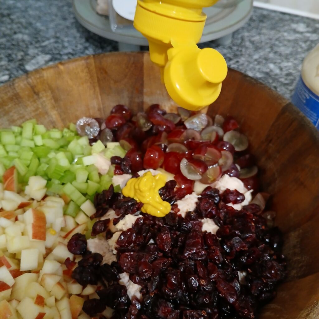 Pouring mustard in a bowl with chicken salad ingredients