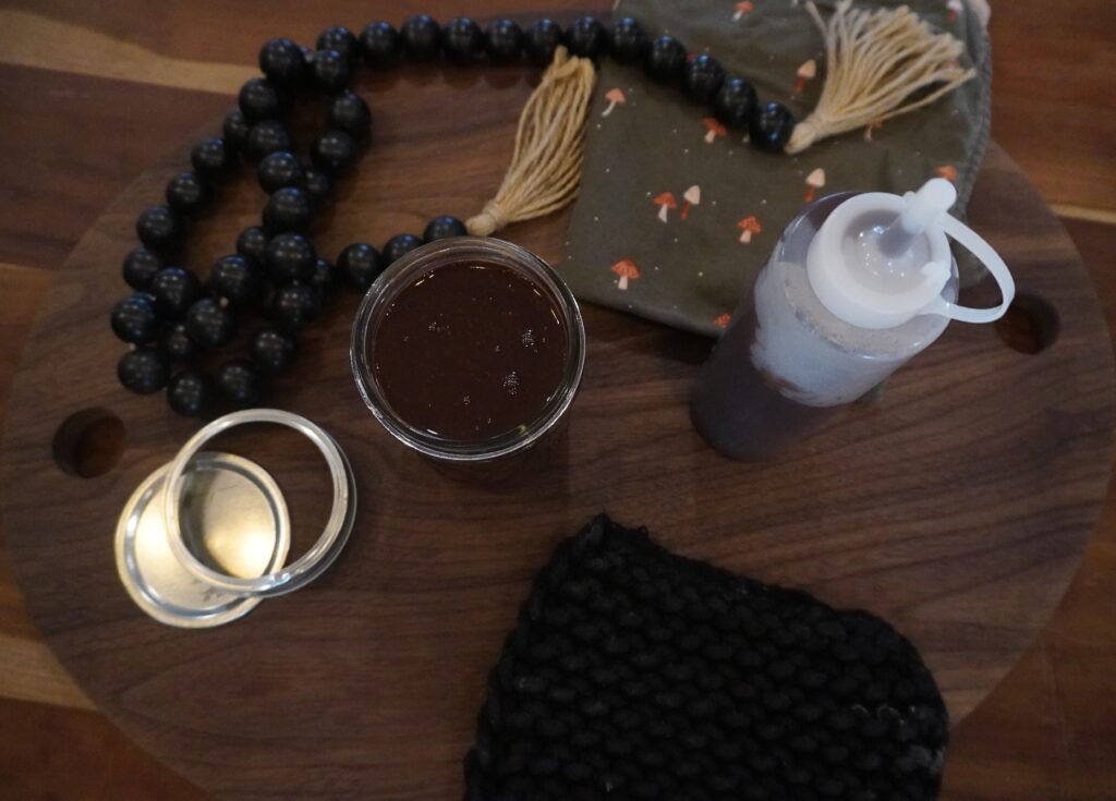 Chocolate syrup in a jar and plastic bottle staged on a wooden cutting board with black beads and a lid