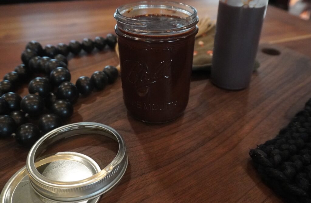 Chocolate syrup in a jar with mason jar lid, beads and a plastic bottle of chocolate syrup